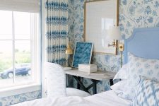 a delicate blue bedroom with floral wallpaper walls, a blue bed with blue and white bedding, blue floral curtains and a small vanity