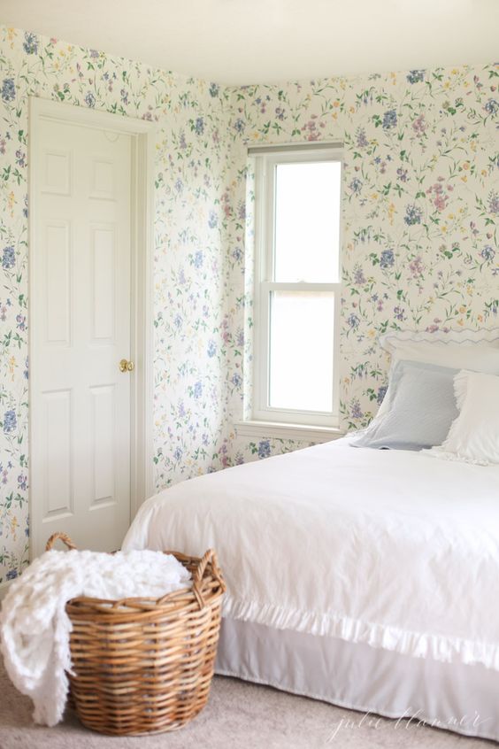 a delicate pastel bedroom with floral wallpaper all over, a bed, neutral and pastel bedding, a basket with some bedding