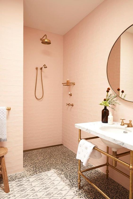 A delicate peachy pink bathroom clad with tiles, a terrazzo floor, a free standing sink and a round mirror is very soft