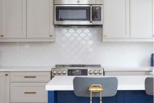 a dove grey kitchen with shaker cabinets, a bold blue kitchen island, white countertops, a white scallop tile backsplash and lamps