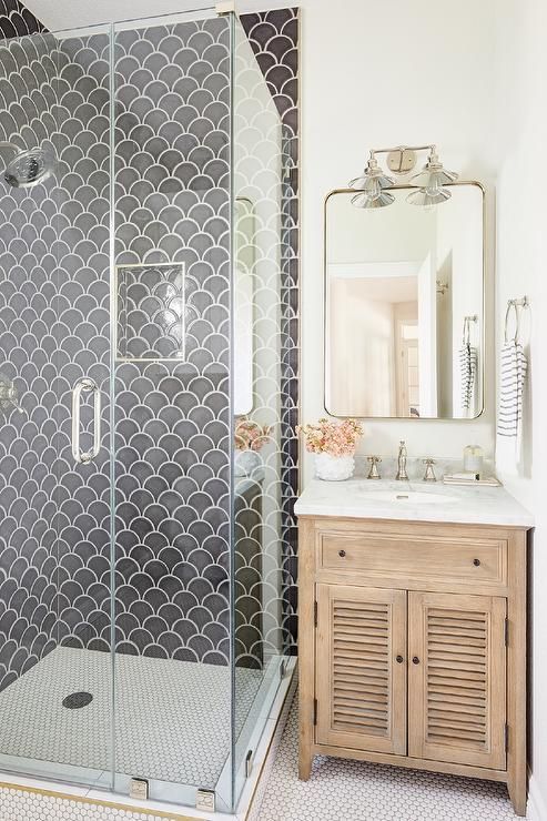 a farmhouse bathroom with grey scallop tiles and white penny ones, a stained vanity and a mirror with lights
