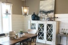 a farmhouse dining room with taupe walls and shiplap, a white glass cabinet, a stained table and upholstered chairs