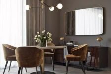 a glam and chic taupe dining room with a round table, rust-colored chairs, a glossy floating credenza and a large mirror