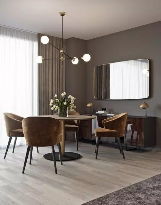 a glam and chic taupe dining room with a round table, rust-colored chairs, a glossy floating credenza and a large mirror