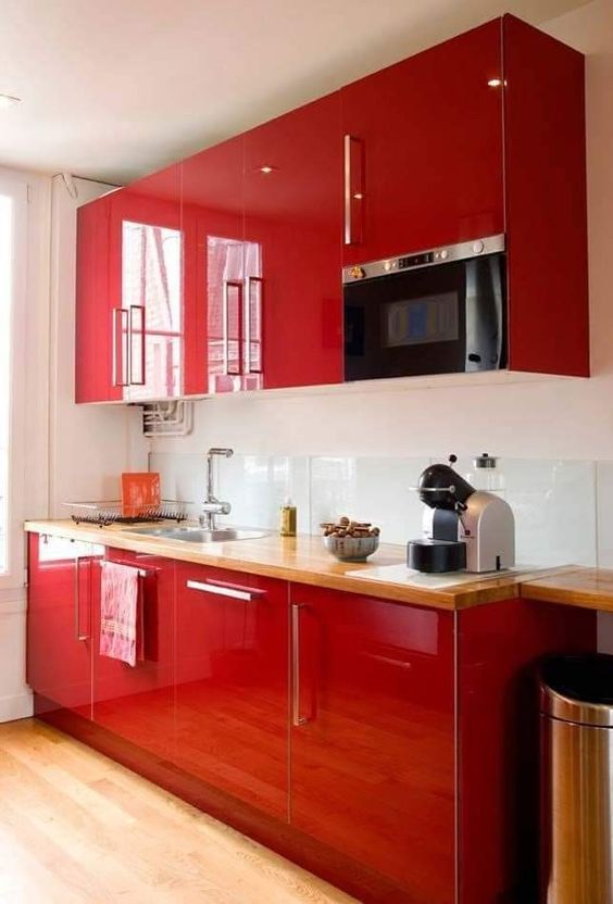 A glossy red kitchen with a clear glass backsplash and butcherblock countertops, built in appliances is wow