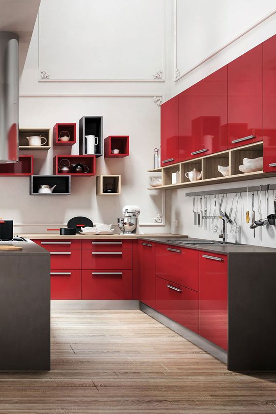 A glossy red kitchen with grey countertops, a white backsplash and eye catchy colorful box shelves