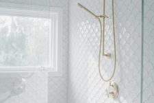 a gorgeous white bathroom clad with fishscale tiles, a shower space with a window, gold fixtures is elegant and cool