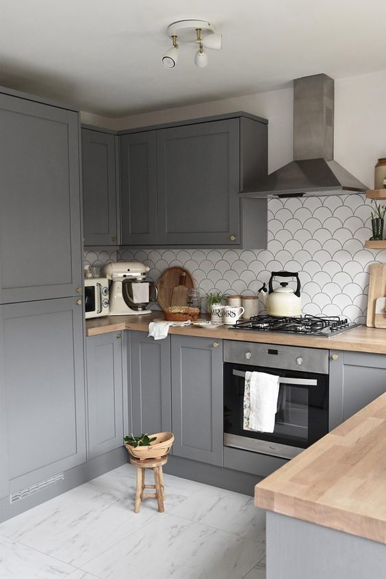 a grey Scandinavian kitchen with a white fish scale tile backsplash, butcherblock countertops and a stainless steel appliances