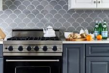 a grey and white kitchen with white countertops and a grey fish scale tile backsplash plus stainless steel appliances