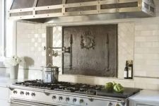 a grey kitchen with tan tiles, a large metal hood and a kitchen island with a metal countertop