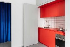 a hidden red kitchen with a white tile backsplash and red grout and large doors to hide it off when not in need