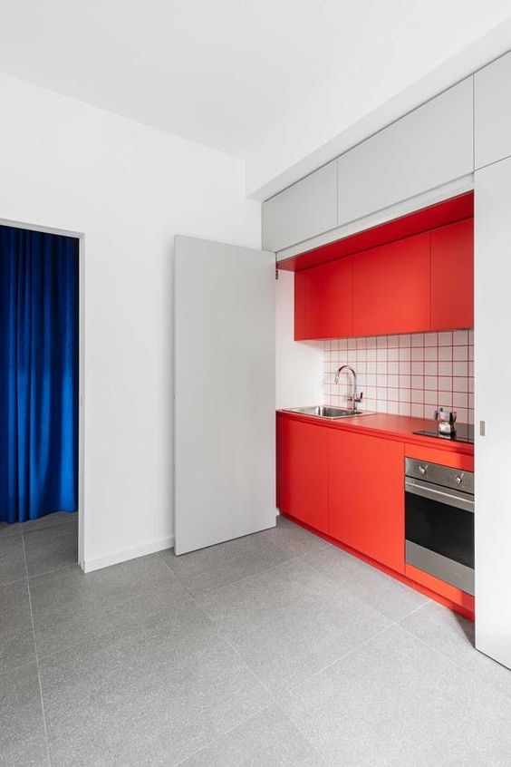 a hidden red kitchen with a white tile backsplash and red grout and large doors to hide it off when not in need