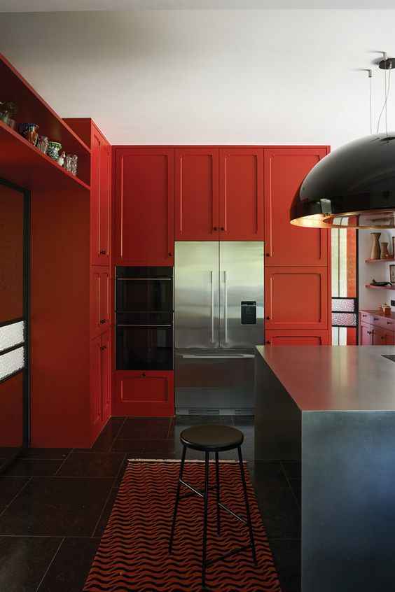 a jaw-dropping deep red kitchen with shaker cabinets, a stone kitchen island, black pendant lamps and stools