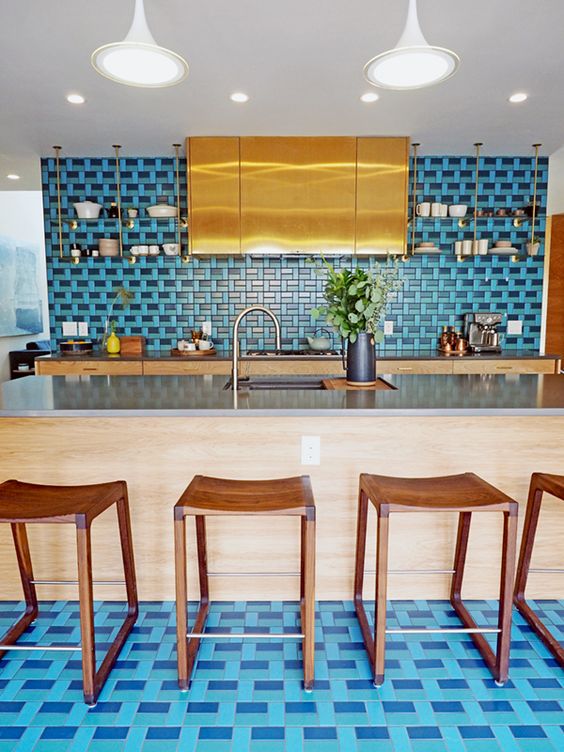 A jaw dropping kitchen with tan cabinets, a large polished gold hood, a bold blue backsplash and a matching floor