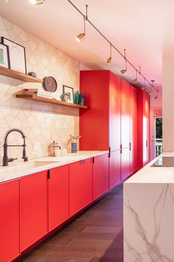 a jaw-dropping matte red kitchen with a geo tile backsplash, a white stone kitchen island, spotlights and some decor