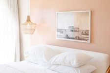 a laconic and bright bedroom with a Peach Fuzz accent wall, a white bed, a woven pendant lamp and some drapes