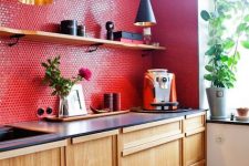 a light-stained kitchen with black countertops, a red penny tile backsplash and black pendant lamps and blooms