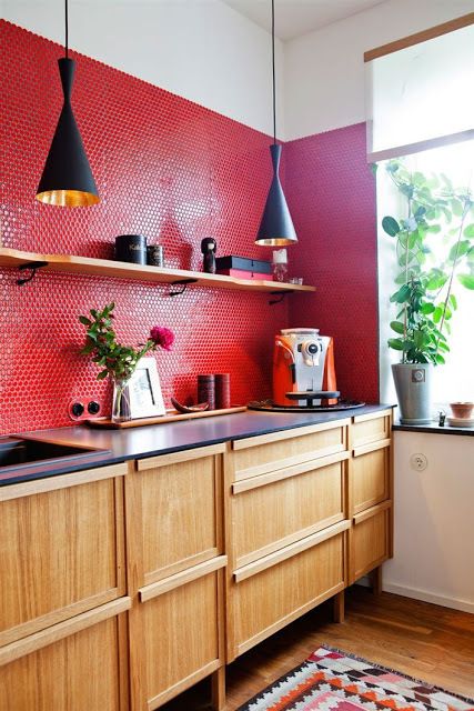 A light stained kitchen with black countertops, a red penny tile backsplash and black pendant lamps and blooms
