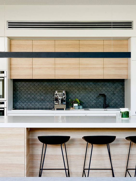 A light stained modern kitchen with matte soot fish scale tiles on the backsplash and white stone countertops