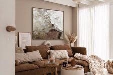 a lovely and inviting living room with a beige accent wall, a brown sofa, a stool and a pouf and a pendant lamp