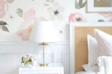 a lovely bedroom with a watercolor floral wall, a bed with a rattan headboard, white nightstands, gold touches