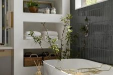 a mid-century modern bathroom with a window, a wall clad with black tiles, a wall with shelves, a tub and a stool