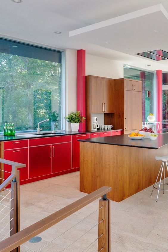 A mid century modern kitchen with bright red and stained cabinets, a large window instead of a backsplash and black countertops