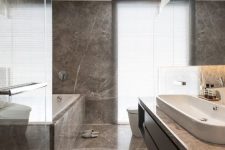 a minimalist bathroom clad with brown marble, with a long sleek vanity and a marble clad bathtub is chic
