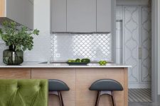 a minimalist kitchen with matte grey and stained cabinets, white countertops and a white fish scale tile backsplash, tall stools
