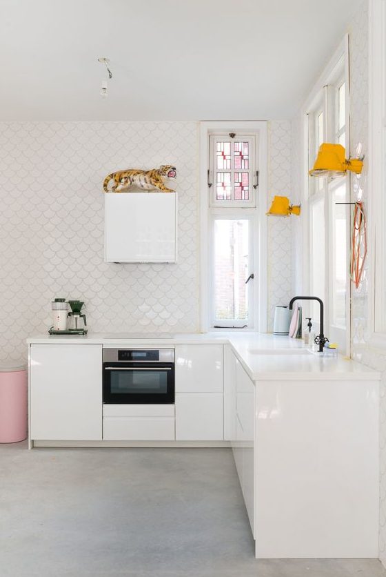 a minimalist white kitchen with glossy cabinets, white stone countertops, white scallop tile walls, yellow lamps and pink touches