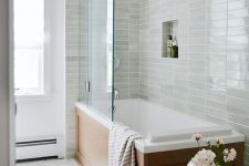 a modern bathroom with a light green stacked tile in the bathtub space, a white hex tile floro and some lovely decor