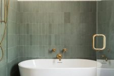 a modern bathroom with white and green stacked tiles, an oval tub, a wooden stool and brass fixtures