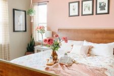 a modern bedroom with a Peach Fuzz accent wall, a stained bed with printed bedding, a nightstand, a tassel chandelier and some blooms