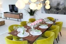 a modern dining room with a stained table, chartreuse chairs, a bubble chandelier and some art