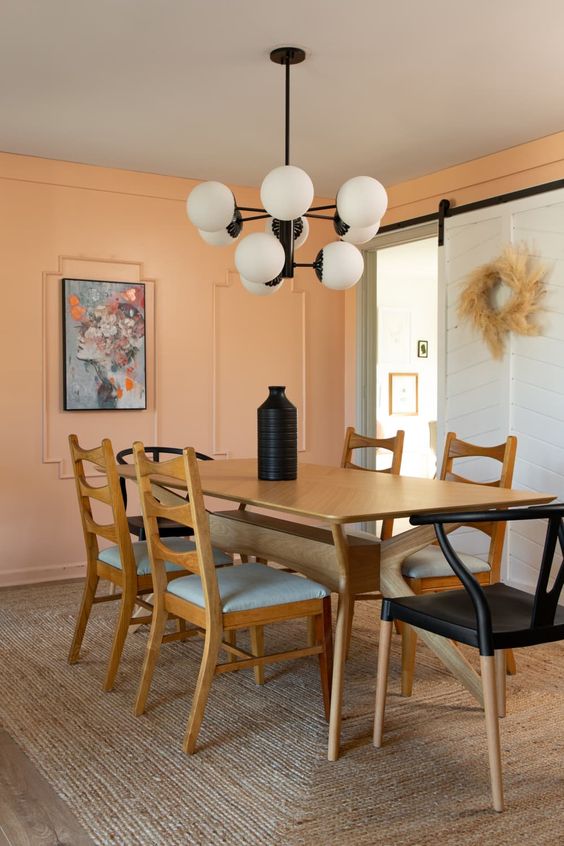 a modern dining room with a stained table, mismatching chairs, a chandelier and a bright artwork