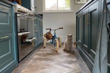 a modern farmhouse kitchen with navy cabinets, a herringbone floor, some decor and a gorgeous cat