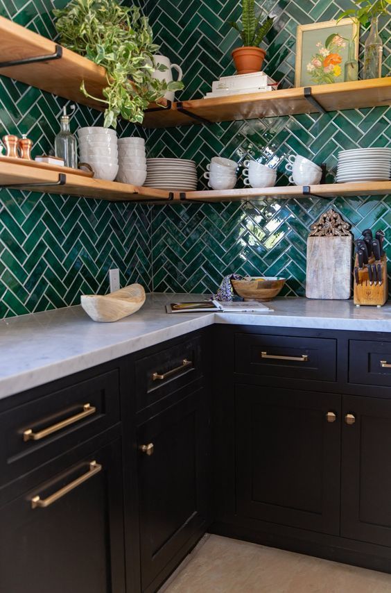 a modern farmhouse kitchen with navy cabinets, a white stone countertop, an emerald herringbone tile backsplash, open shelves, potted plants