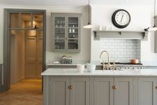 a modern farmhouse kitchen with white walls and a light-stained herringbone floor, a grey kitchen island, a white backsplash and pendant lamps
