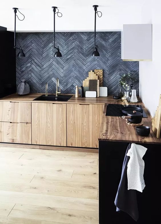a modern kitchen with MDF cabinets, a grey herringbone tile backsplash, black pendant lamps and greenery