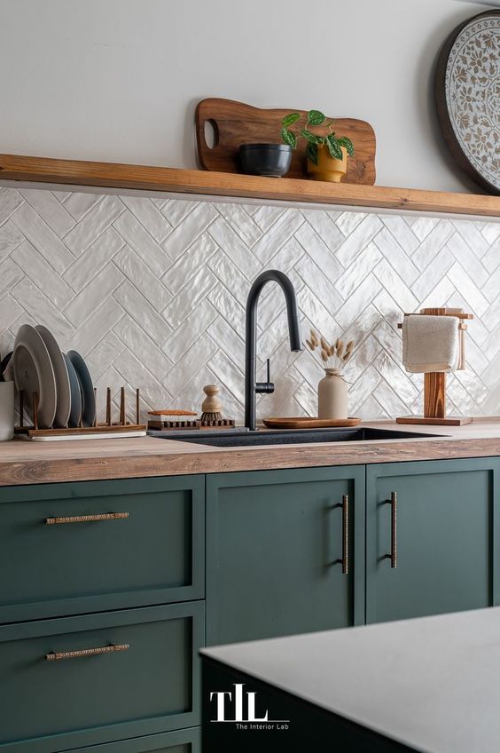 a modern kitchen with dark green cabinets, butcherblock countertops, a white herringbone tile backsplash, an open shelf