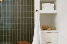 a modern serene bathroom with a shower space clad with green stacked tiles, built-in shelves and a cabinet and some baskets