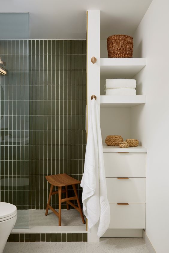 A modern serene bathroom with a shower space clad with green stacked tiles, built in shelves and a cabinet and some baskets