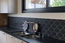 a monochromatic kitchen with black countertops, black frames and a black fishscale tile backsplash to make the space cohesive
