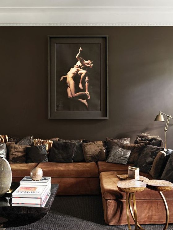 A moody and exquisite liivng room with dark brown walls, a rust colored sofa and pillows, a coffee table and some lamps