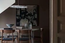 a moody deep brown  dining space with a neutral floor, an oval hairpin leg table, black chairs and a pendant lamp