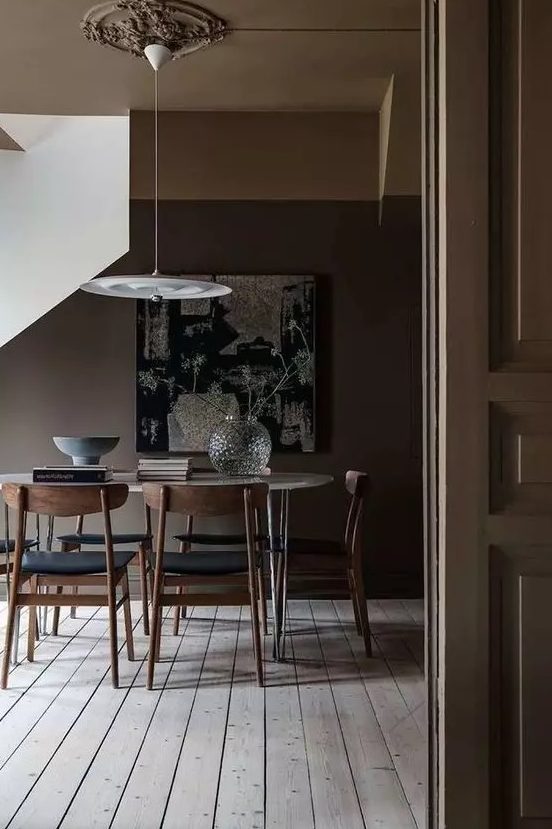 a moody deep brown  dining space with a neutral floor, an oval hairpin leg table, black chairs and a pendant lamp