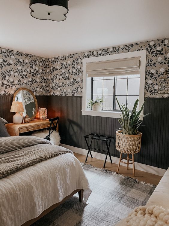 a moody farmhouse bedroom with floral wallpaper, dark fluting, a bed with neutral bedding, a vanity and a small chair