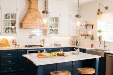 a navy and white kitchen with a white tile backsplash and countertops, a light-stained wooden hood for an accent