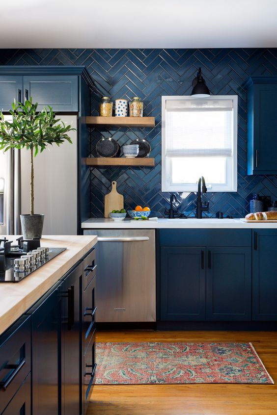 a navy farmhouse kitchen with shaker cabinets, white stone countertops, open shelves, a a fridge and some greenery