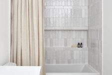 a neutral bathroom clad with white and grey stacked tiles, with white appliances and a neutral shower curtain is cool